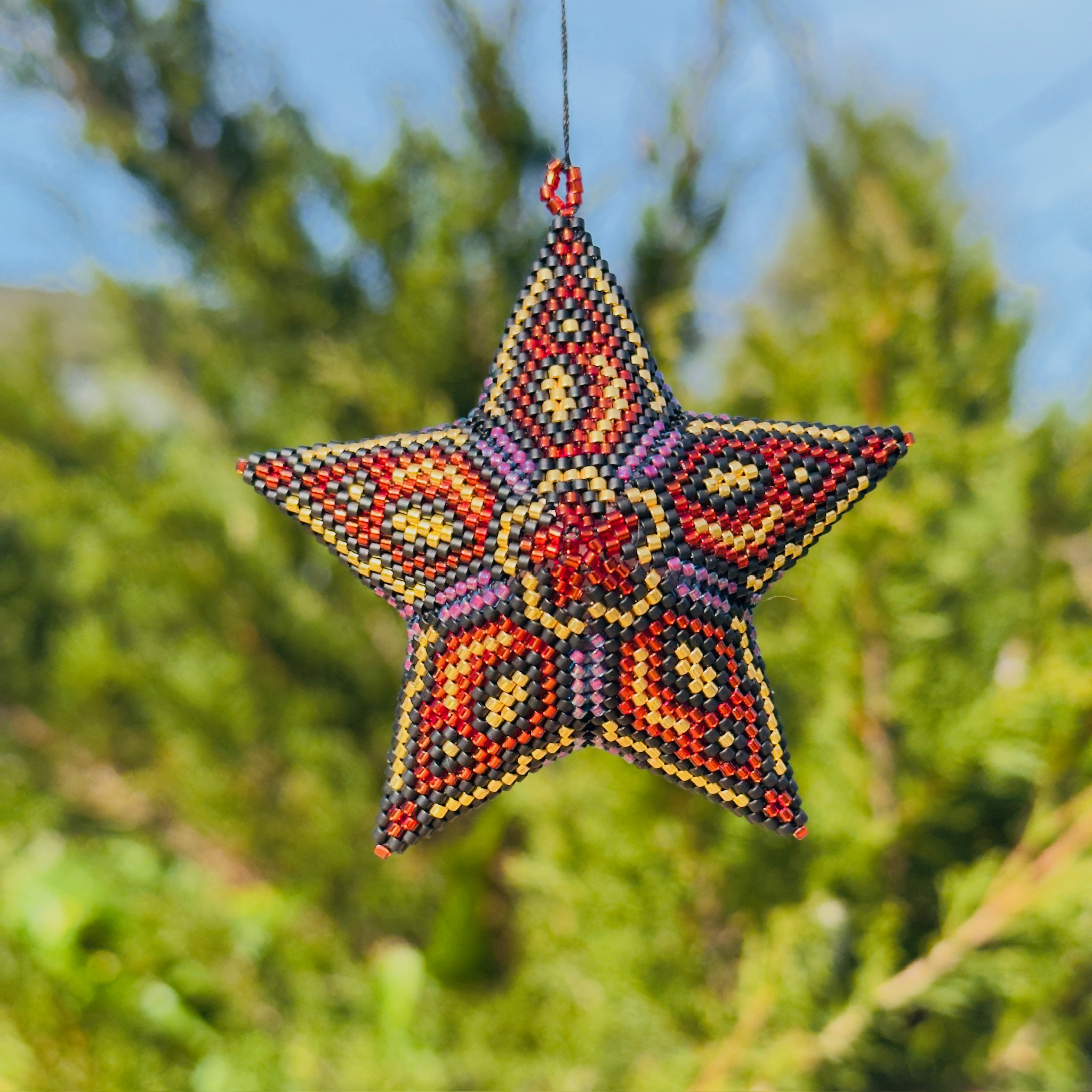 Beaded star ornament with vibrant red, gold, and pink geometric pattern hanging outdoors